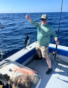 Angler holding caught blue runner fish on fishing boat deck over ocean water