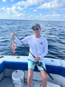 Angler holding freshly caught grey snapper on fishing boat in open ocean waters