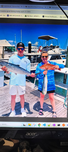 Two anglers displaying freshly caught king mackerel on marina dock with boats in background