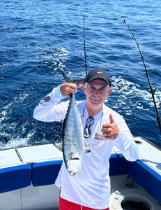 Angler holding freshly caught Little Tunny fish on fishing boat in blue ocean waters