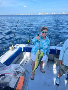 Angler holding fresh caught mahi mahi on fishing boat deck with ocean and city skyline in background