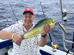 Freshly caught mahi mahi being held on fishing boat with ocean water and fishing rods in background