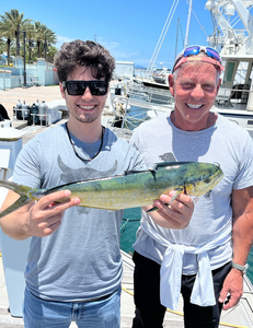 Two anglers holding a fresh caught mahi mahi at a marina dock
