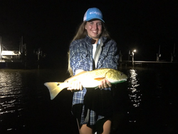 Angler holding caught redfish at night near marina dock