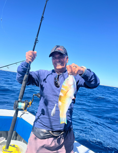 Angler holding freshly caught fish on fishing boat in open ocean waters