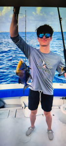 Angler holding caught Queen Triggerfish on fishing boat deck over ocean waters
