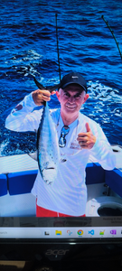 Angler on fishing boat holding fishing rod over blue ocean water giving thumbs up