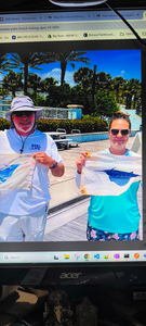 Two anglers displaying their fishing catch on a boat deck with palm trees in background