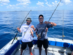 Two anglers displaying their catch on a fishing boat in blue ocean waters