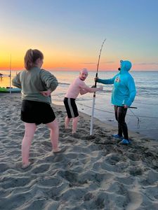 Three people fishing together on beach at sunset in Cape May NJ