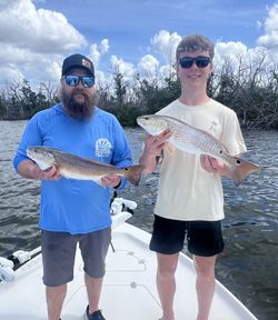 Two anglers displaying caught redfish on fishing boat in Fort Myers FL waters