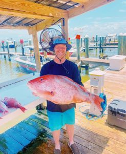 Large red snapper catch displayed at Gulf Shores AL fishing dock with marina and boats in background