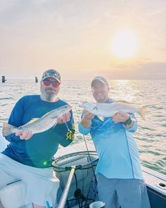 Two anglers displaying speckled trout catch on fishing boat in Gulf Shores AL waters at sunset