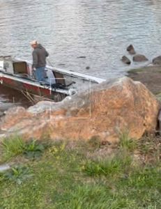 Fishing boat docked near rocky shoreline in Cotter AR with calm water