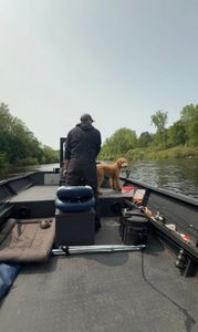 Fishing boat on river in Fruitport MI with dog on deck surrounded by trees