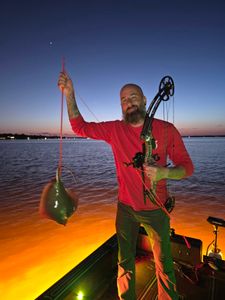 Bowfisher with compound bow holding large stingray catch at Orange Beach AL during twilight