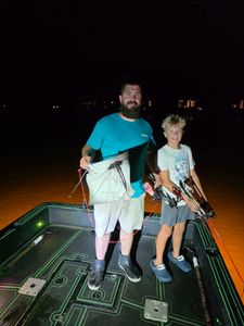Two people on fishing boat at night in Orange Beach AL holding stingrays caught while fishing