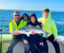 Four people on a fishing boat holding a striped bass catch in Port Monmouth Road NJ waters