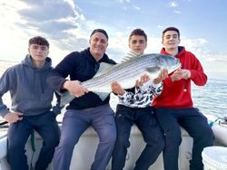 Four anglers displaying caught striped bass on fishing boat in Port Monmouth Road NJ waters