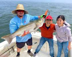 Striped bass caught during fishing trip in Port Monmouth Road NJ with three people celebrating on boat
