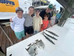 Family fishing trip in Gulf Shores AL displaying catch of spadefish, speckled trout, and king mackerel on cleaning table at marina
