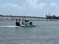 Fishing boat on water near harbor with jetty and larger vessel in Port Aransas TX