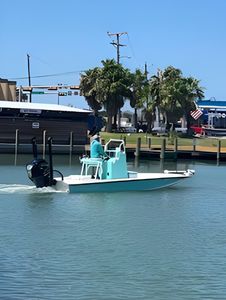 Turquoise fishing boat navigating marina waters in Port Aransas TX with docks and trees in background