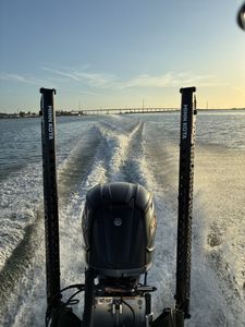 Fishing boat wake trailing behind outboard motor in Port Aransas TX waters with bridge visible in distance