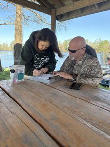 Tour guide signing paperwork at wooden table under pavilion near lake in Orange TX