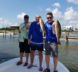 Three anglers displaying caught redfish on fishing boat in Gulf Shores Alabama waters