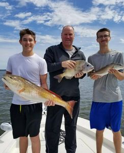 Three anglers displaying caught redfish on fishing boat in Gulf Shores Alabama waters