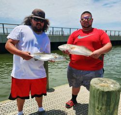 Two anglers displaying caught redfish and speckled trout on fishing dock in Gulf Shores AL