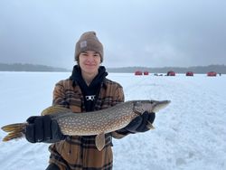 A fisherman holding a large northern pike in Saranac Lake