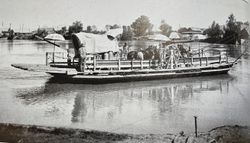Historic black and white photograph of river ferry with covered wagon and paddle wheel at Yuma AZ