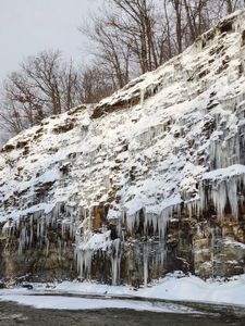 Majestic icicles cascade down the snow-capped cliff, transforming the winter landscape into a breathtaking natural wonder.