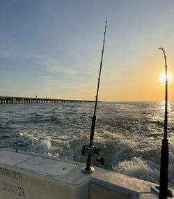 Fishing rods mounted on boat with ocean wake and pier visible during sunset in Norfolk VA