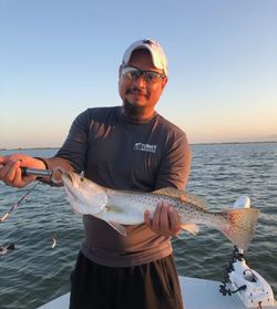 A person fishing in the waters of Corpus Christi, holding a spotted weakfish.