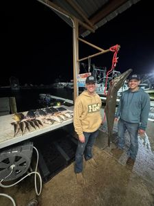 Two anglers displaying massive alligator gar catch at fishing dock in Lafitte Louisiana with smaller fish laid out on cleaning table