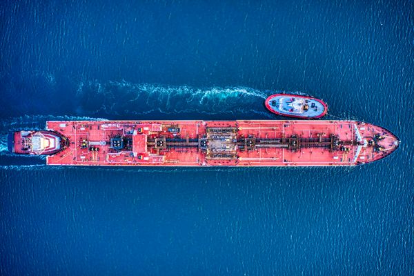 Massive tanker navigates open waters with tugboat assistance.