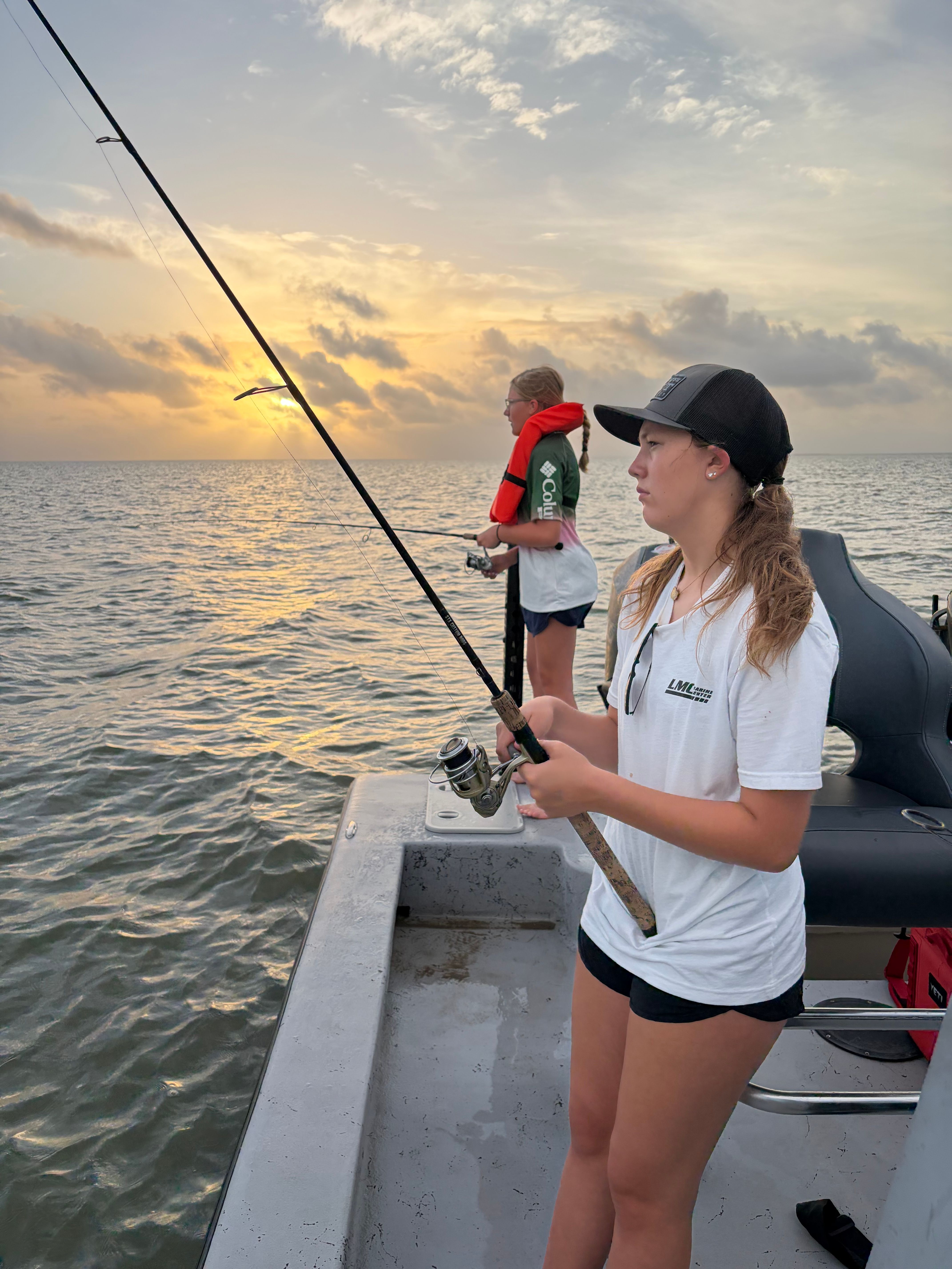 Fishing rod held over ocean water from boat deck during sunset
