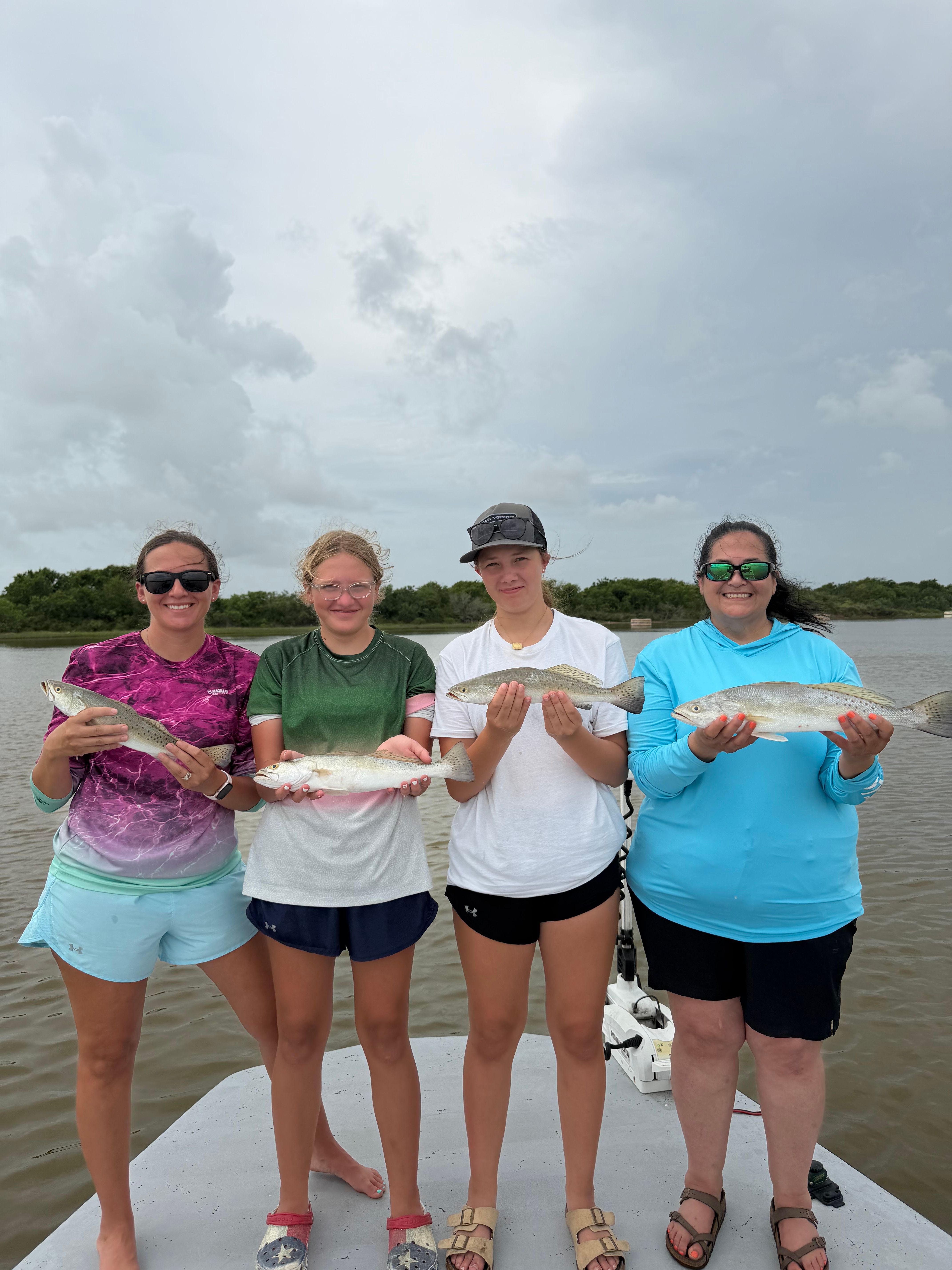 Four anglers displaying their catch of speckled trout during an outdoor fishing trip