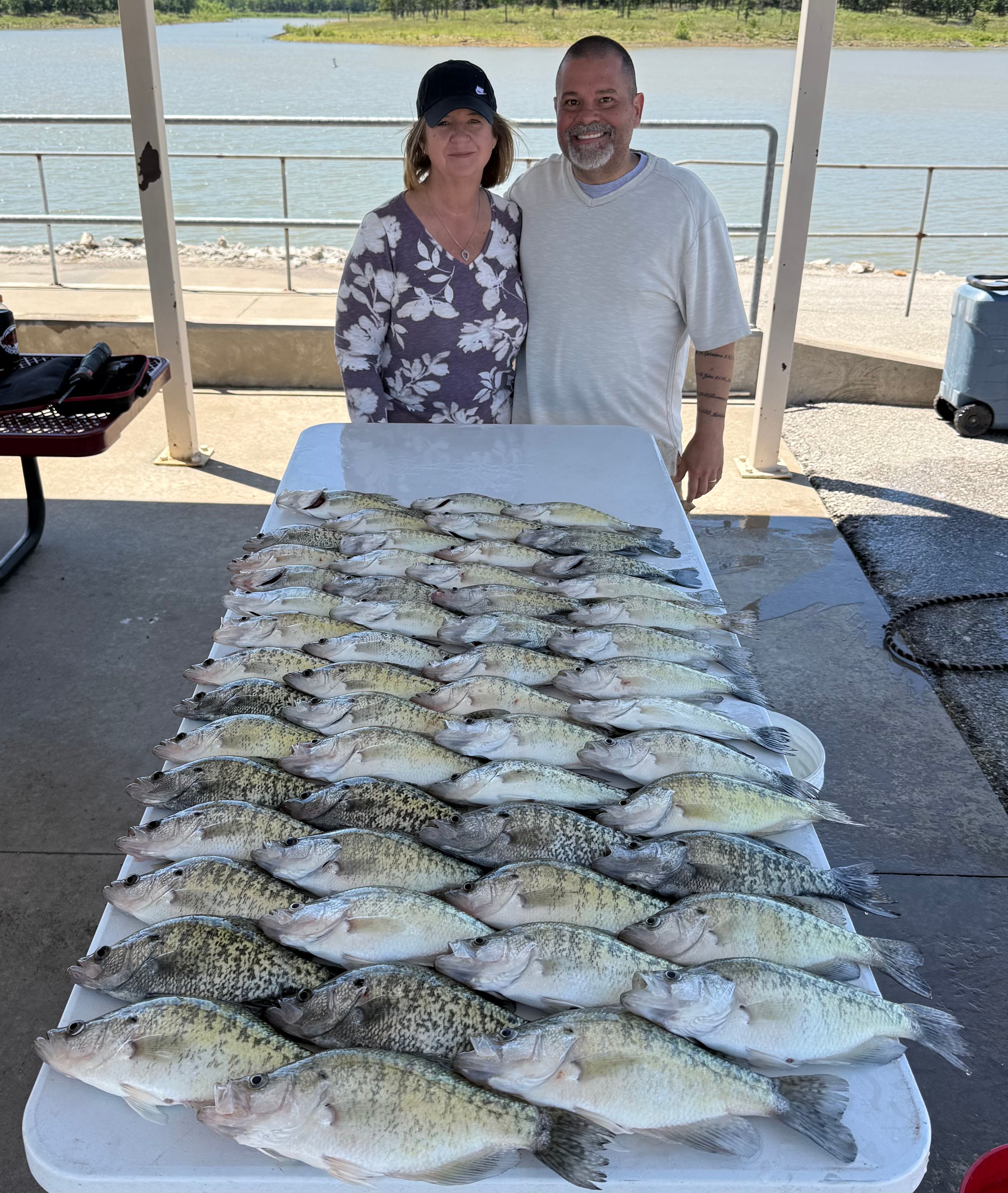 Large catch of crappie fish displayed on cleaning table at outdoor fishing dock