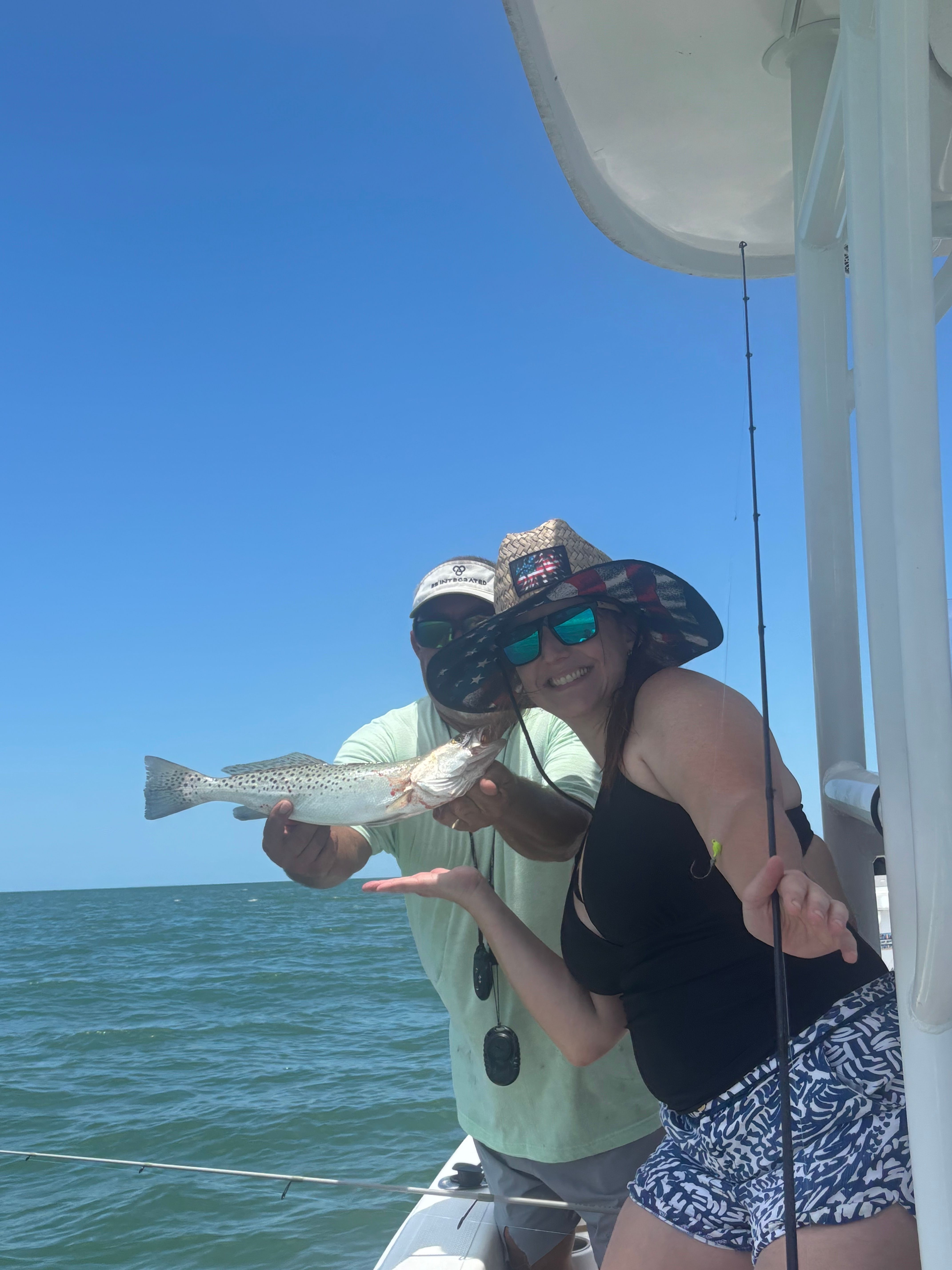 Angler holding caught speckled trout on fishing boat over ocean water