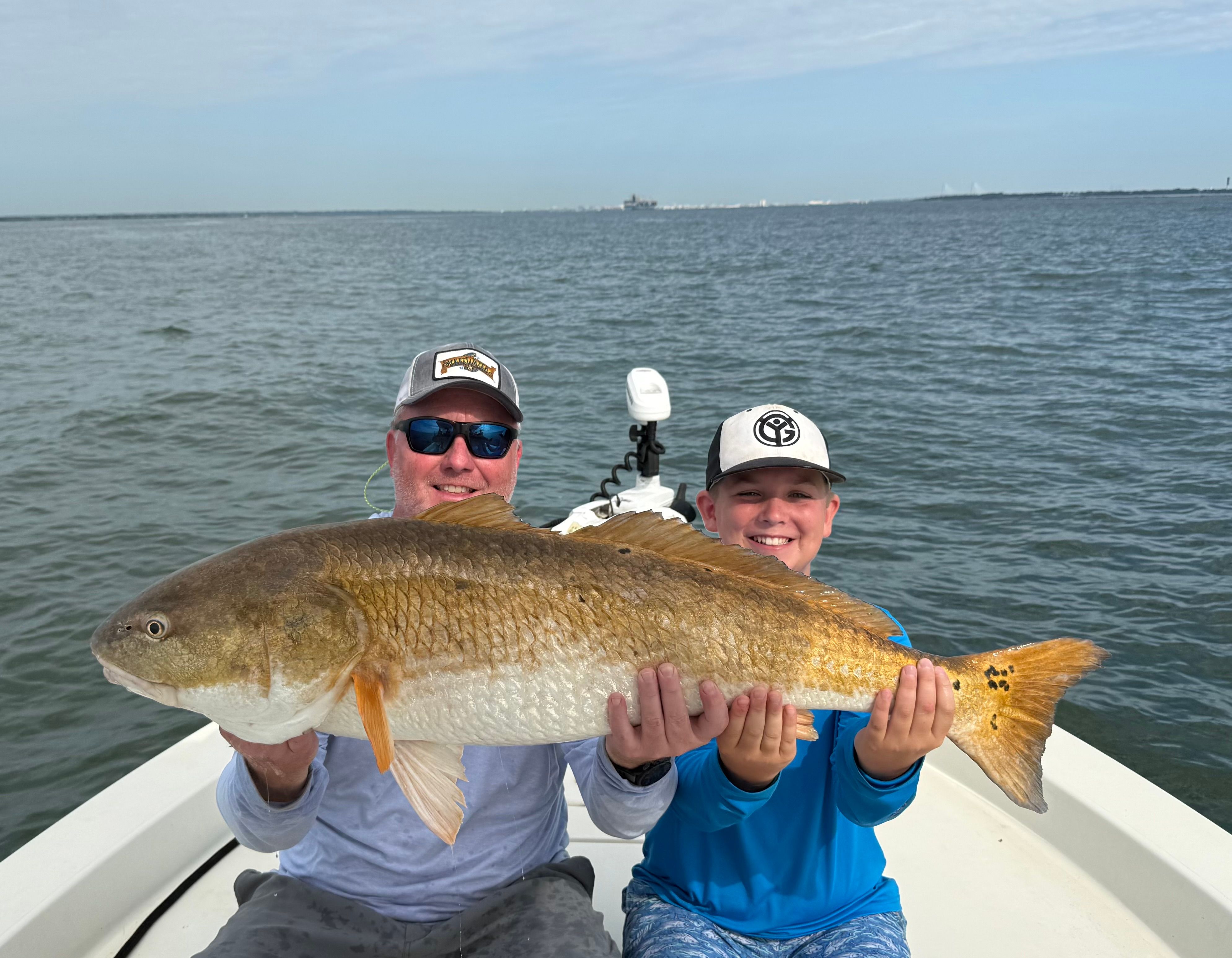 Two anglers holding a large redfish on a boat while fishing on open water