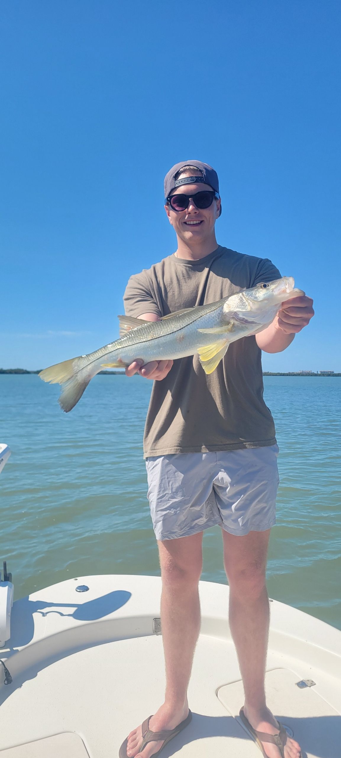 Angler holding caught snook on boat deck with blue sky and water in background