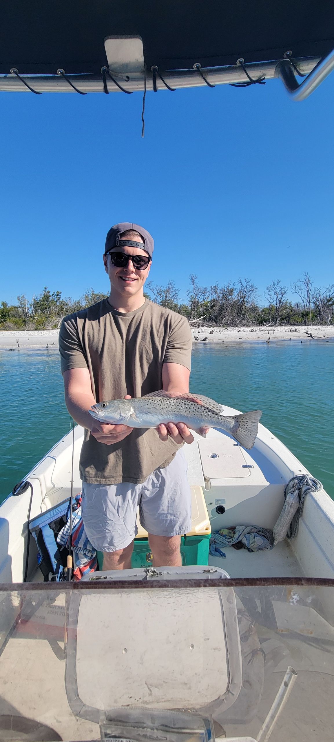 Angler holding freshly caught speckled trout on fishing boat in clear blue water