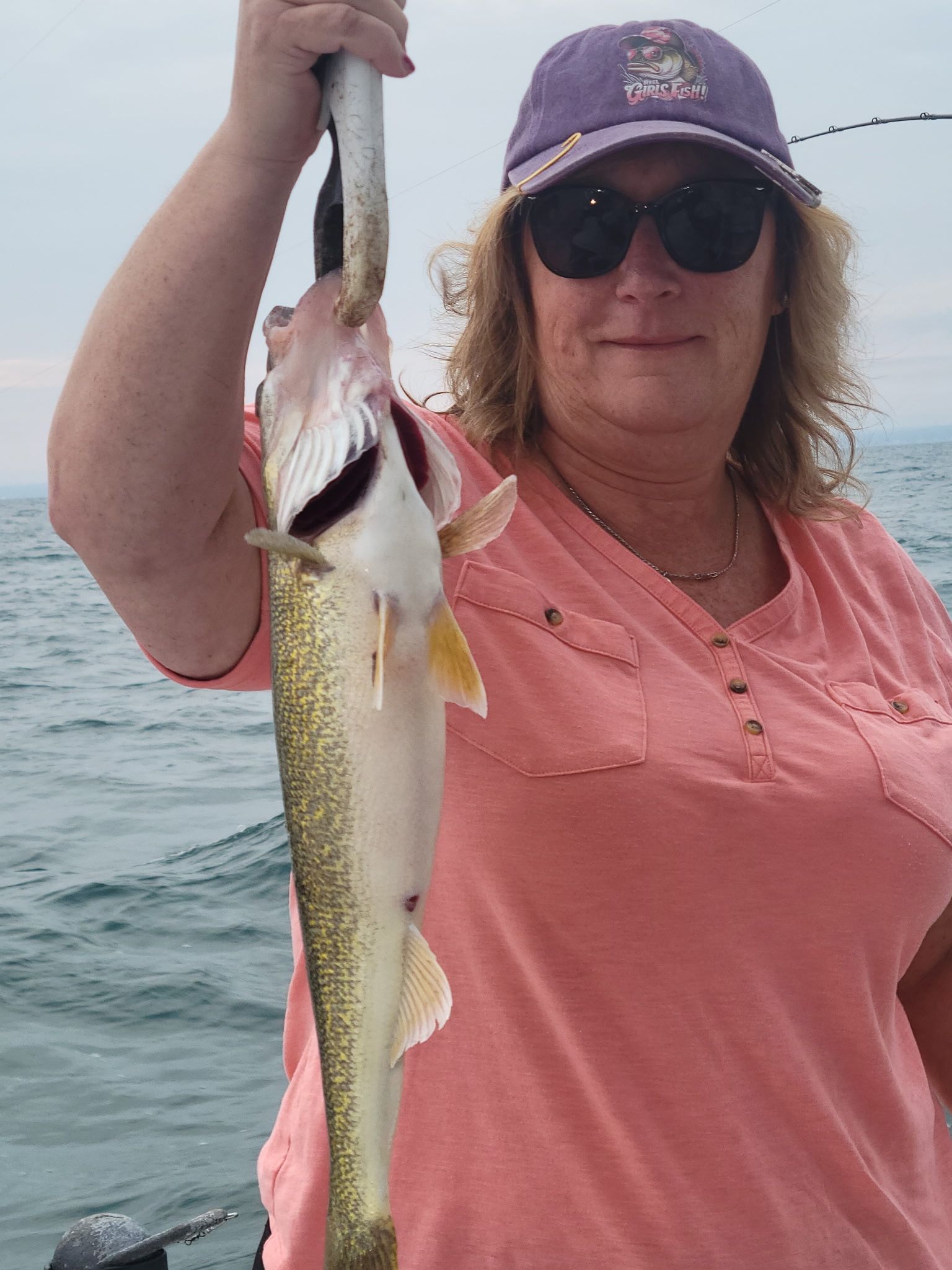 Angler holding freshly caught walleye fish on boat during fishing trip