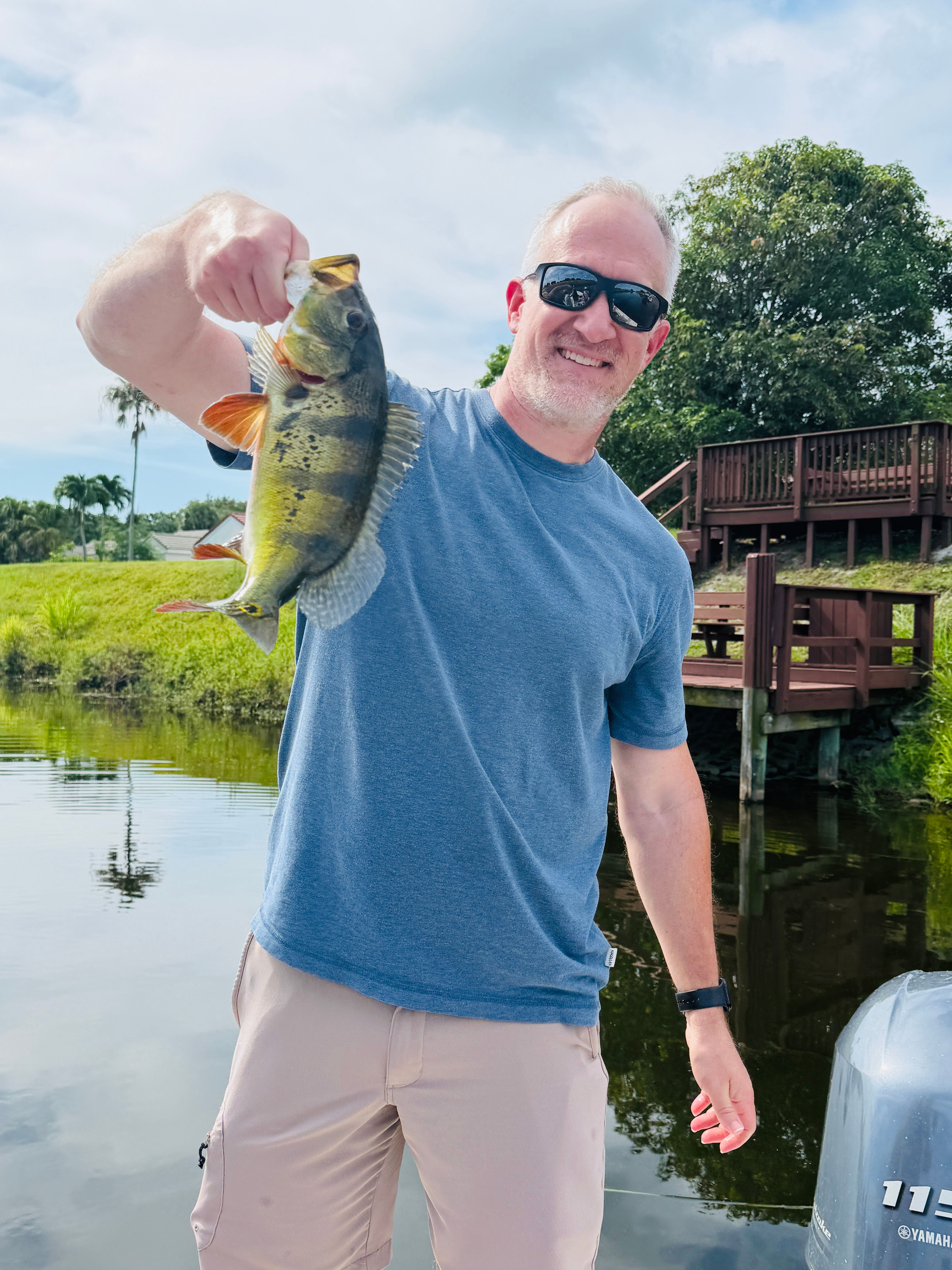 Angler holding caught peacock bass by waterside with wooden dock structure in background