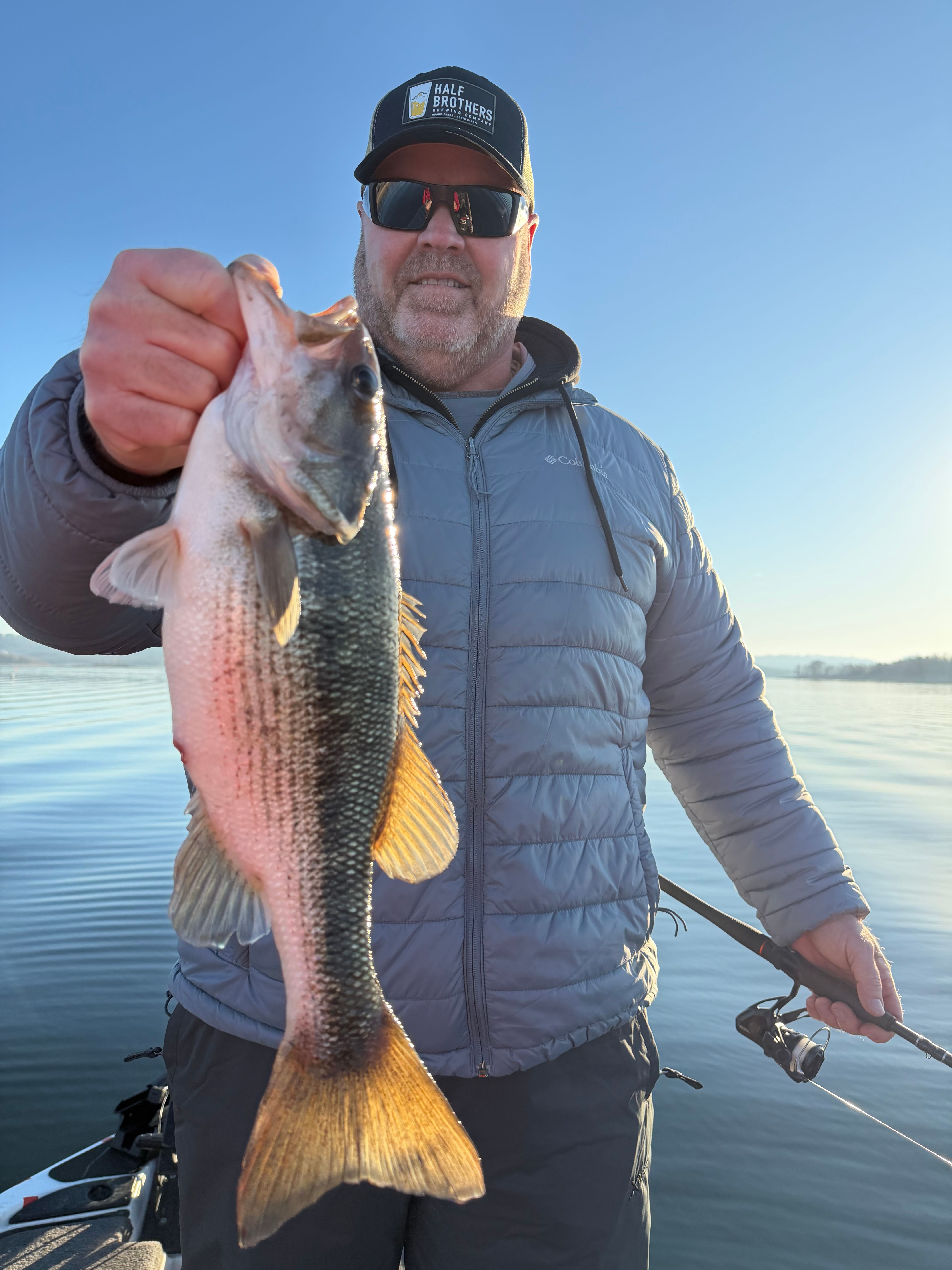 Angler holding a spotted bass caught while fishing on calm water