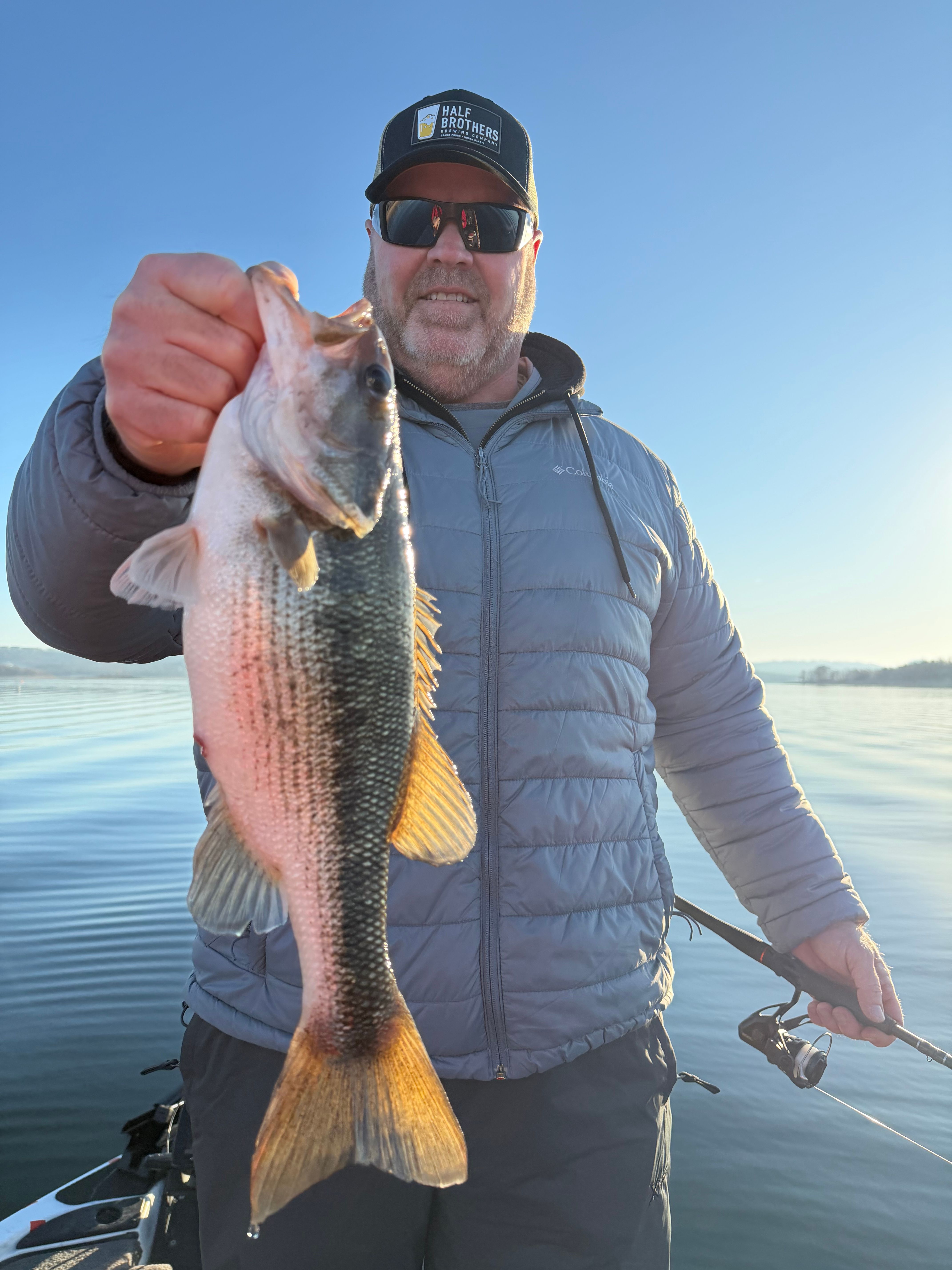 Angler holding spotted bass caught while fishing on calm lake water